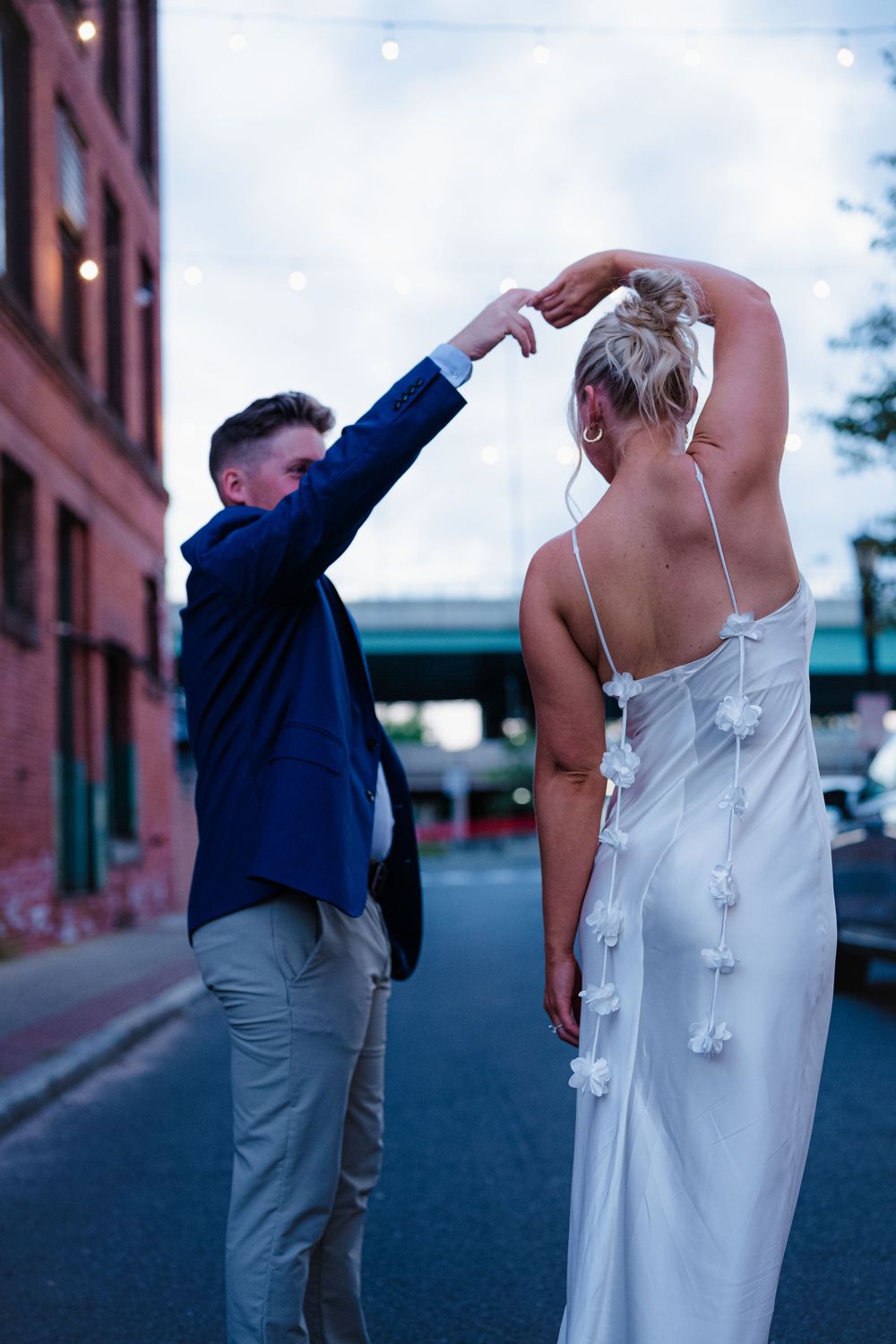 A couple dances playfully in front of an urban brick building during their wedding photoshoot.