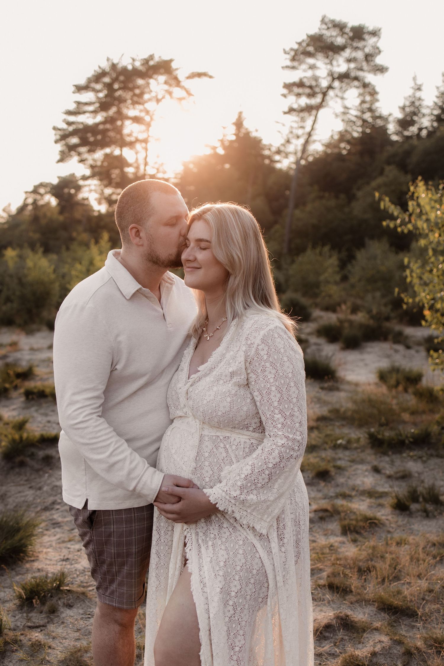 Zwangere vrouw in de armen van haar partner tijdens golden hour shoot.