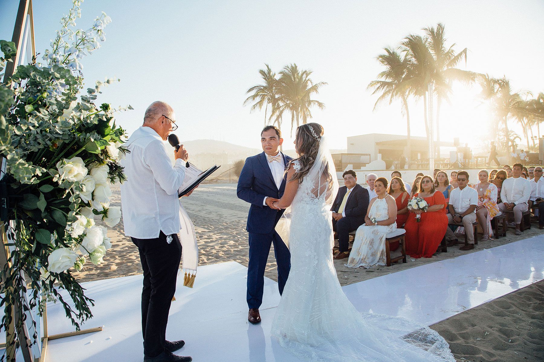 Officiant leads bride and groom in vows at sunset beach wedding ceremony.
