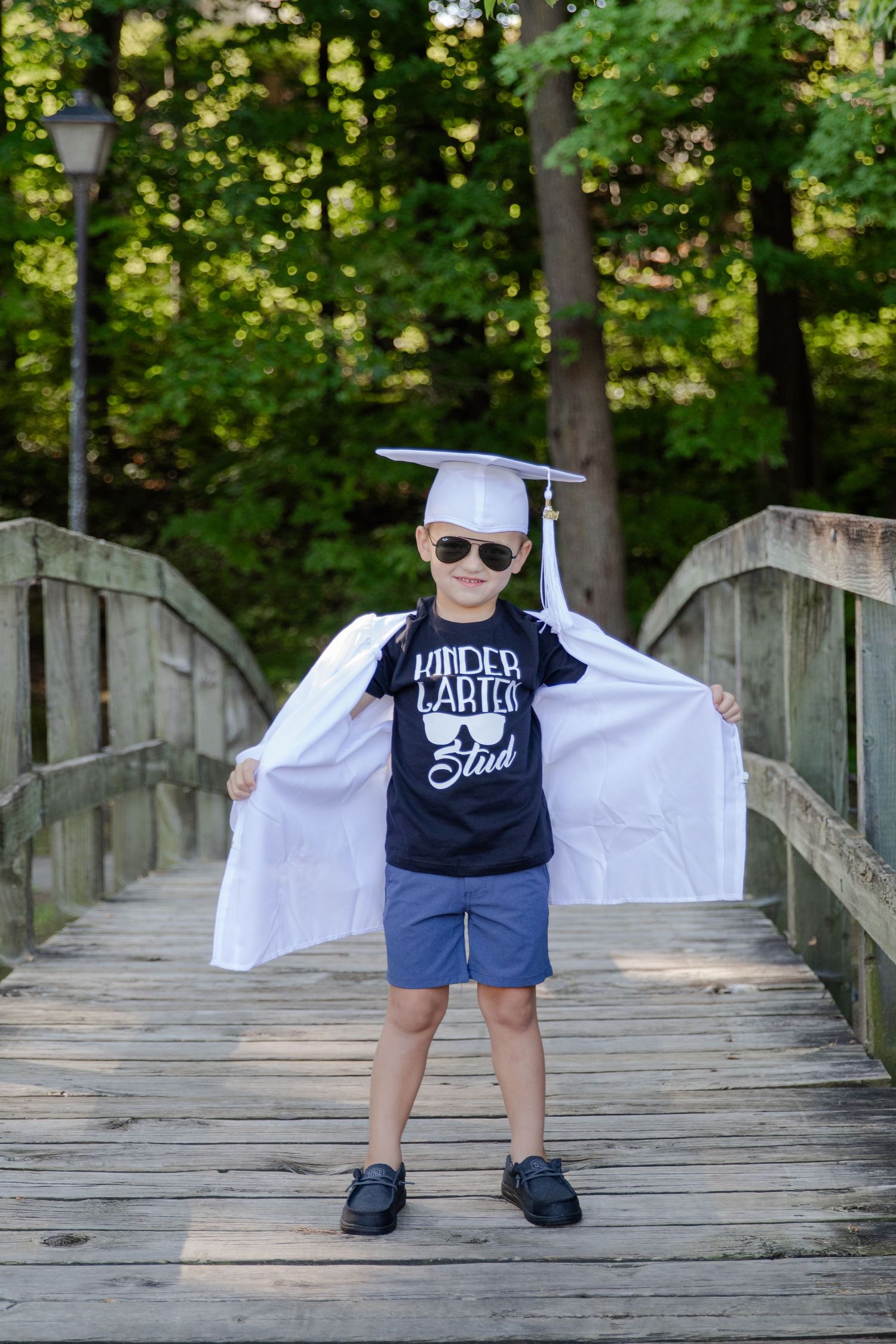 Smiling kindergartener wearing a cap and gown on their first day of school. The child is proud of this milestone.