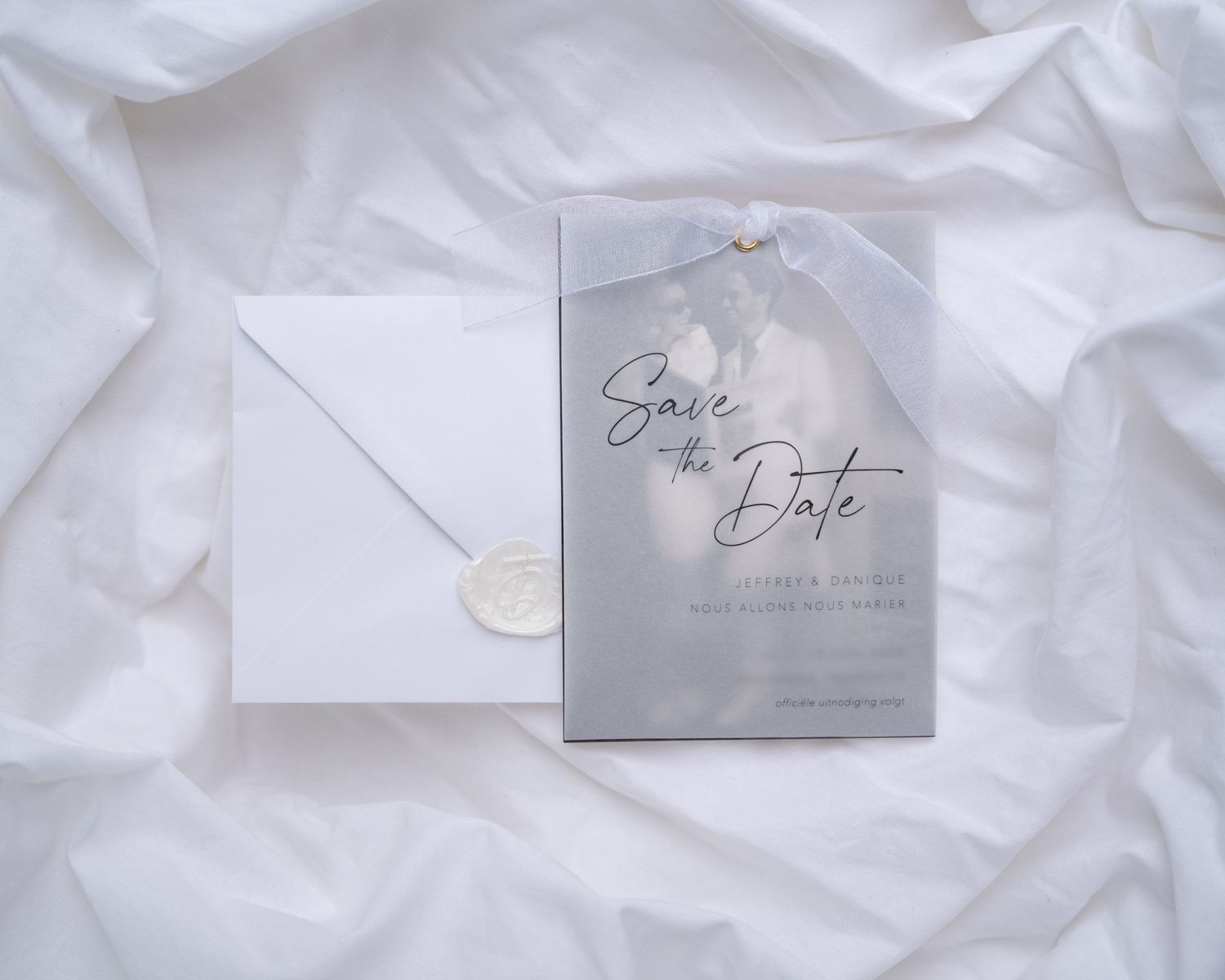 ontwerp voor een save the date kaart. doorzichtig voorvel met de tekst erop gedrukt en een zwart wit foto erachter, samengebonden met lint.