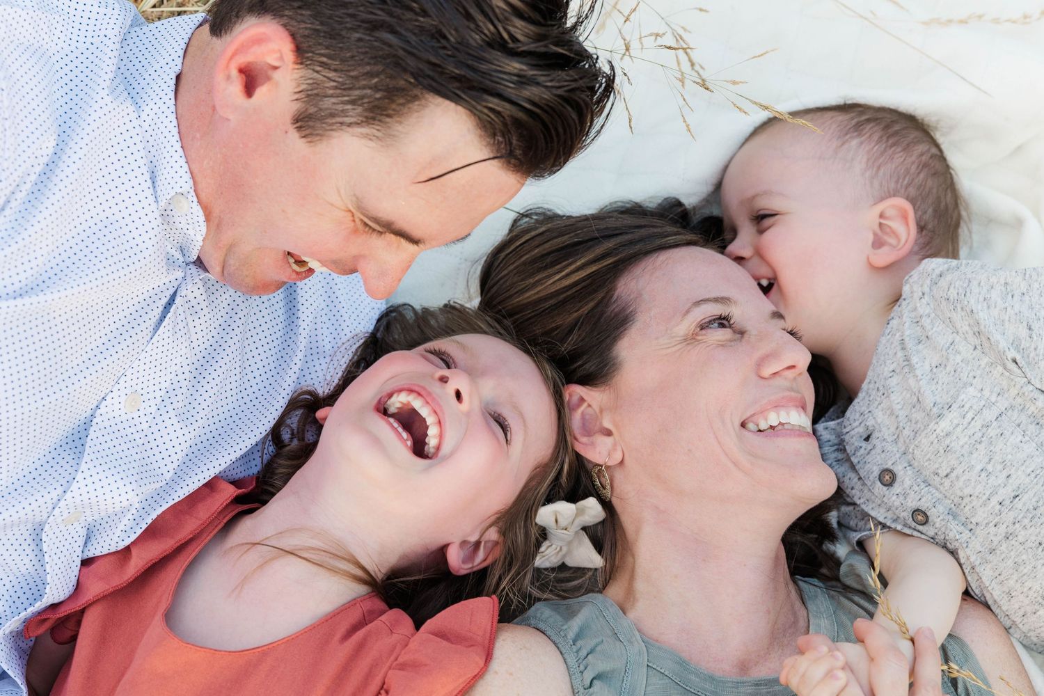 Joyful family of four lying together on a blanket, laughing and sharing a tender moment.