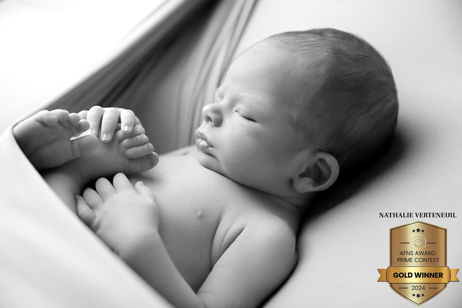 Serene sleeping newborn laying on soft white fabric in black and white photograph.