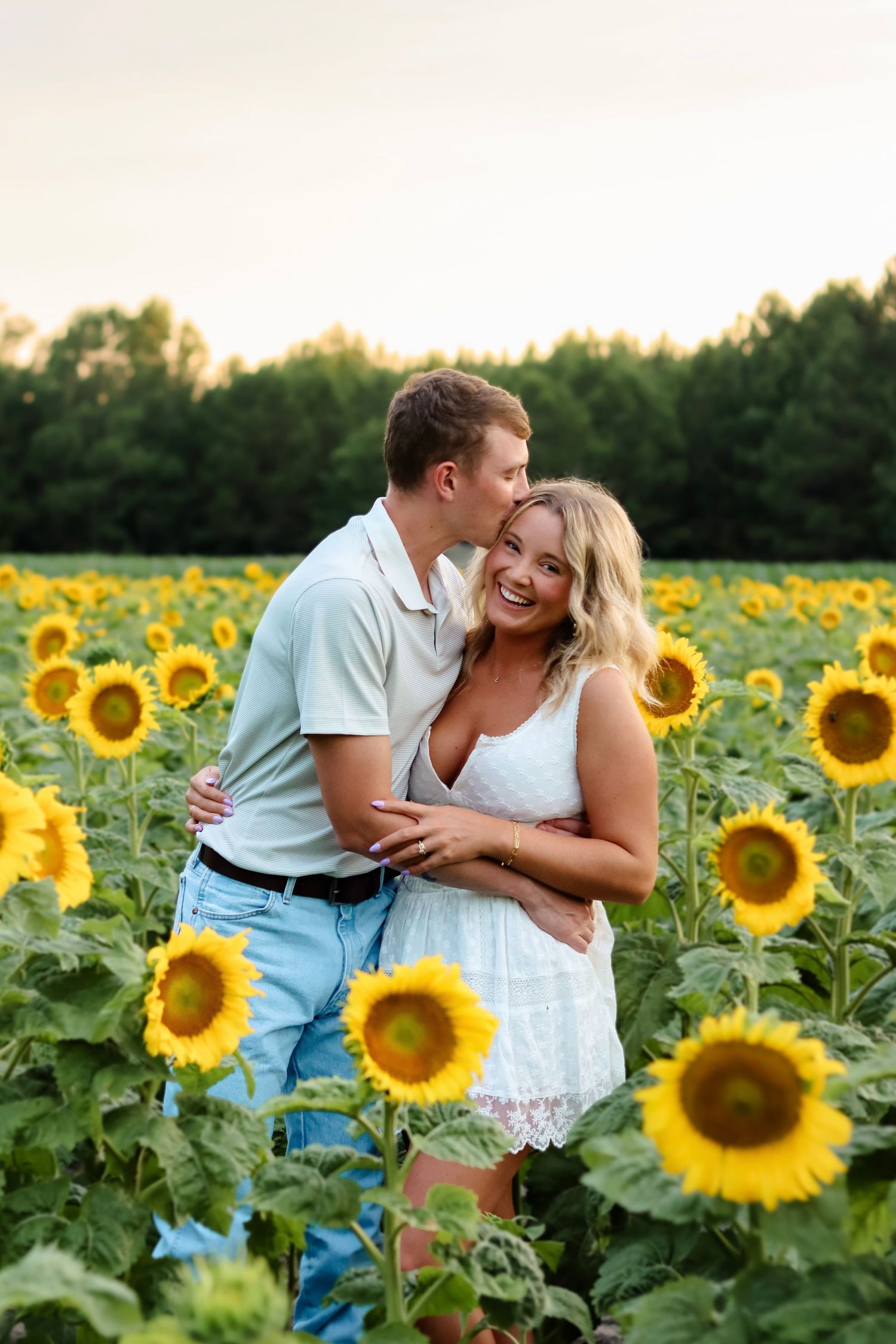 Romantic couple embraces and laughs together in a vibrant sunflower field during sunset.