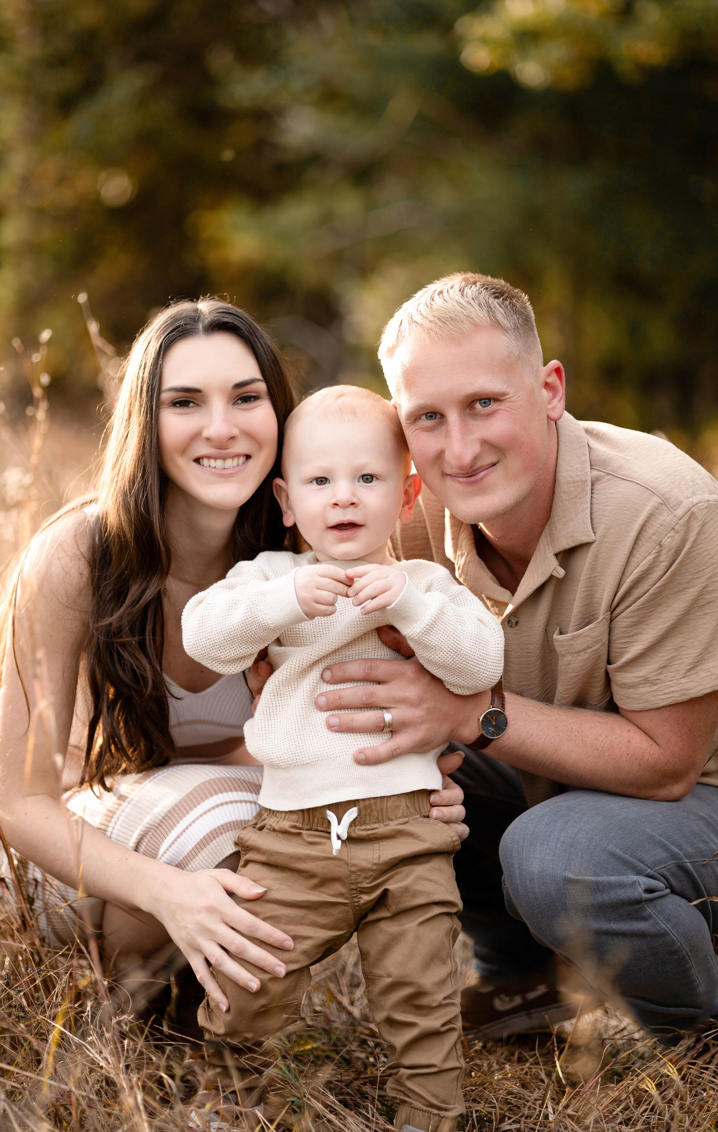 Family of three cuddling together in rustic outdoor setting during golden hour.