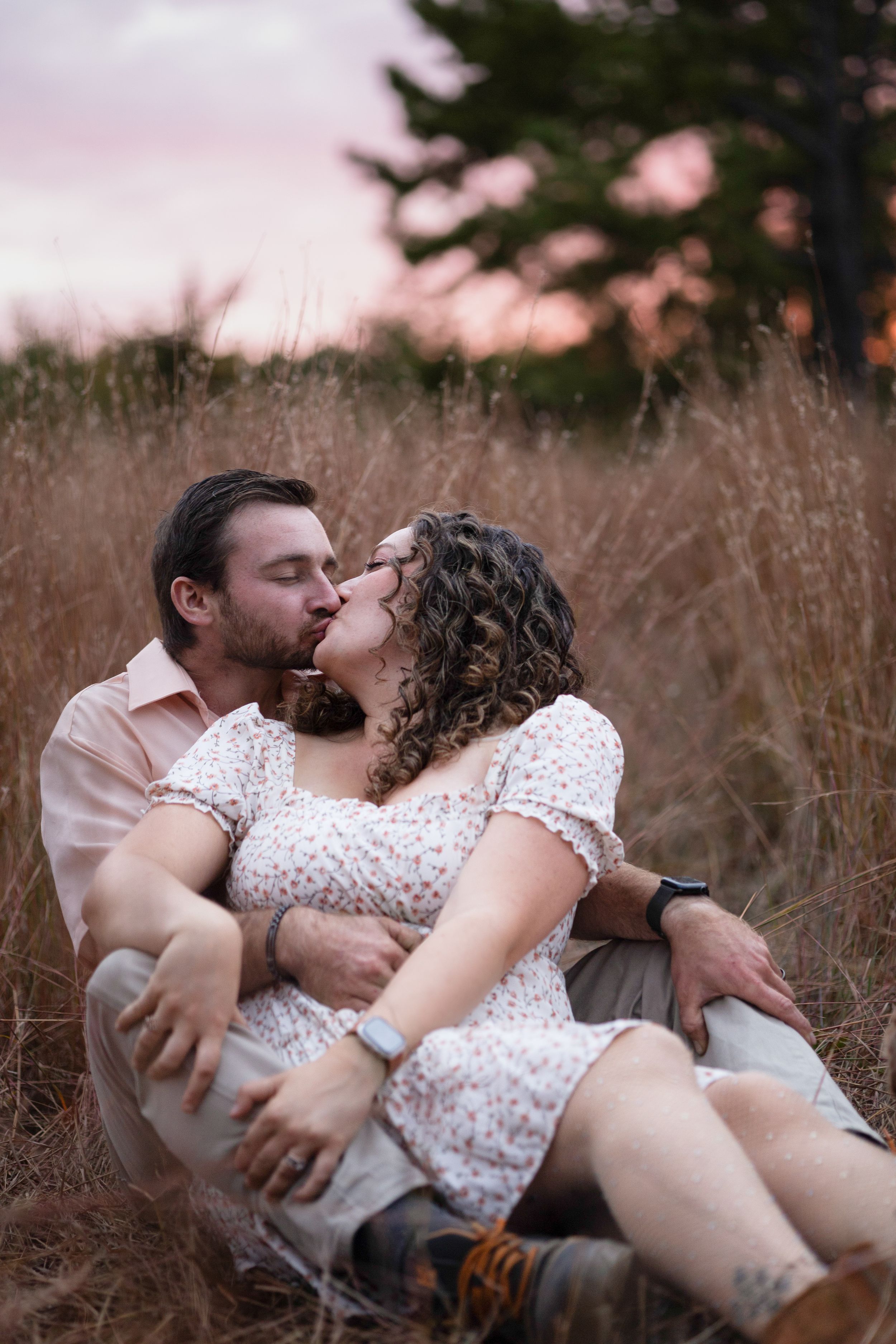 Couple shares intimate moments while lying in tall grass during golden hour.