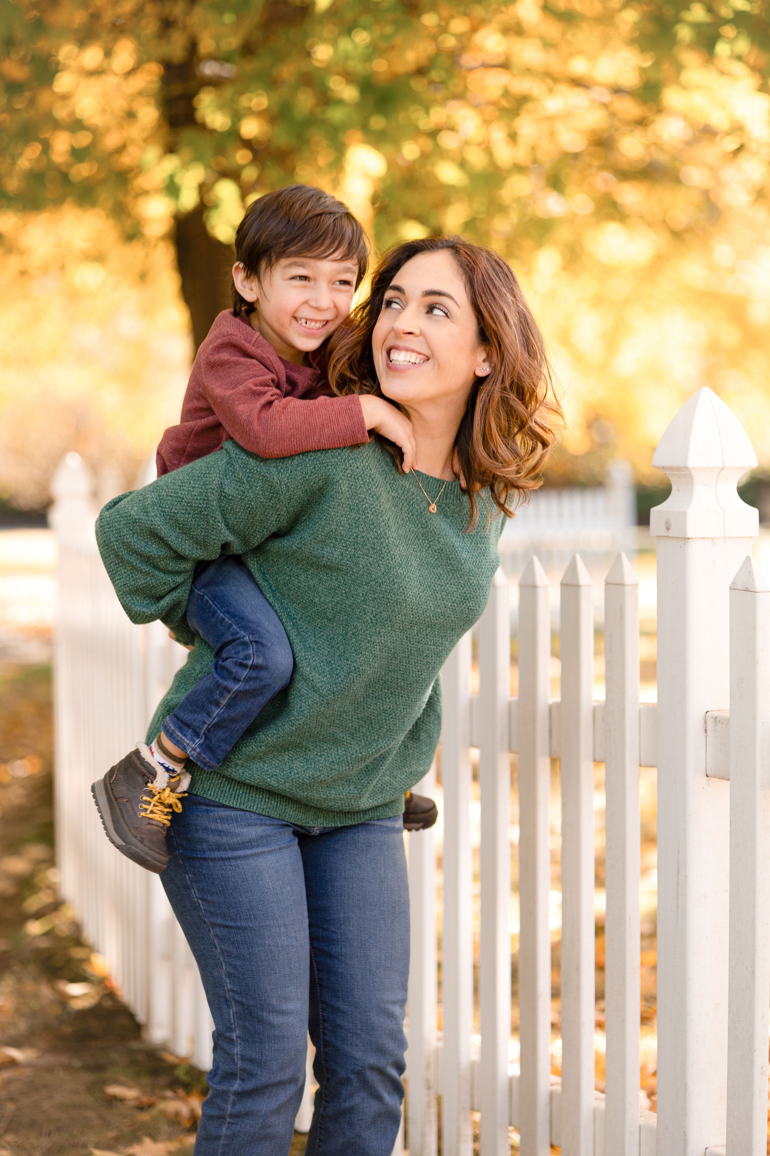 Mother and child play together near white fence during golden autumn afternoon.