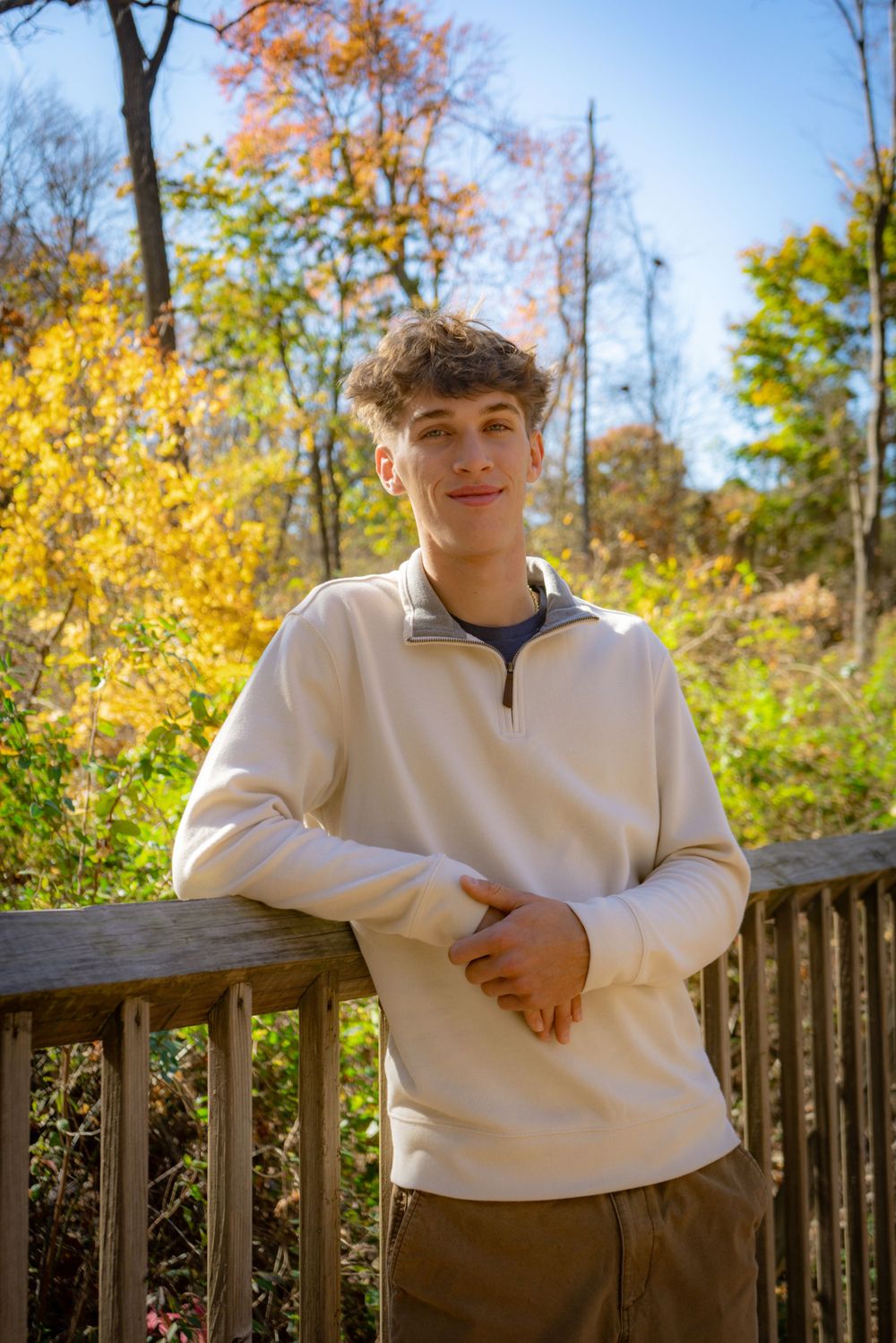 Someone poses casually on a wooden deck surrounded by vibrant fall foliage with yellow and orange leaves.