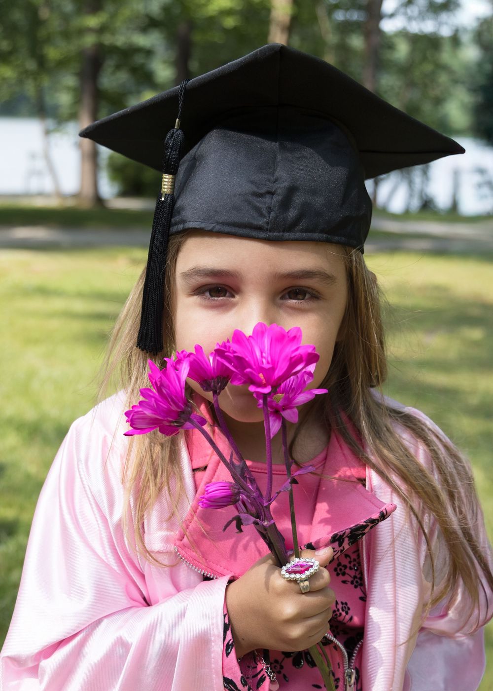 Graduate in pink holding bright magenta daisies during outdoor graduation photoshoot.