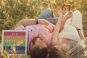 A couple lies on a blanket viewing ultrasound photos with a rainbow book beside them.