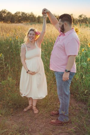 A couple dances in a golden field during sunset, celebrating a pregnancy.