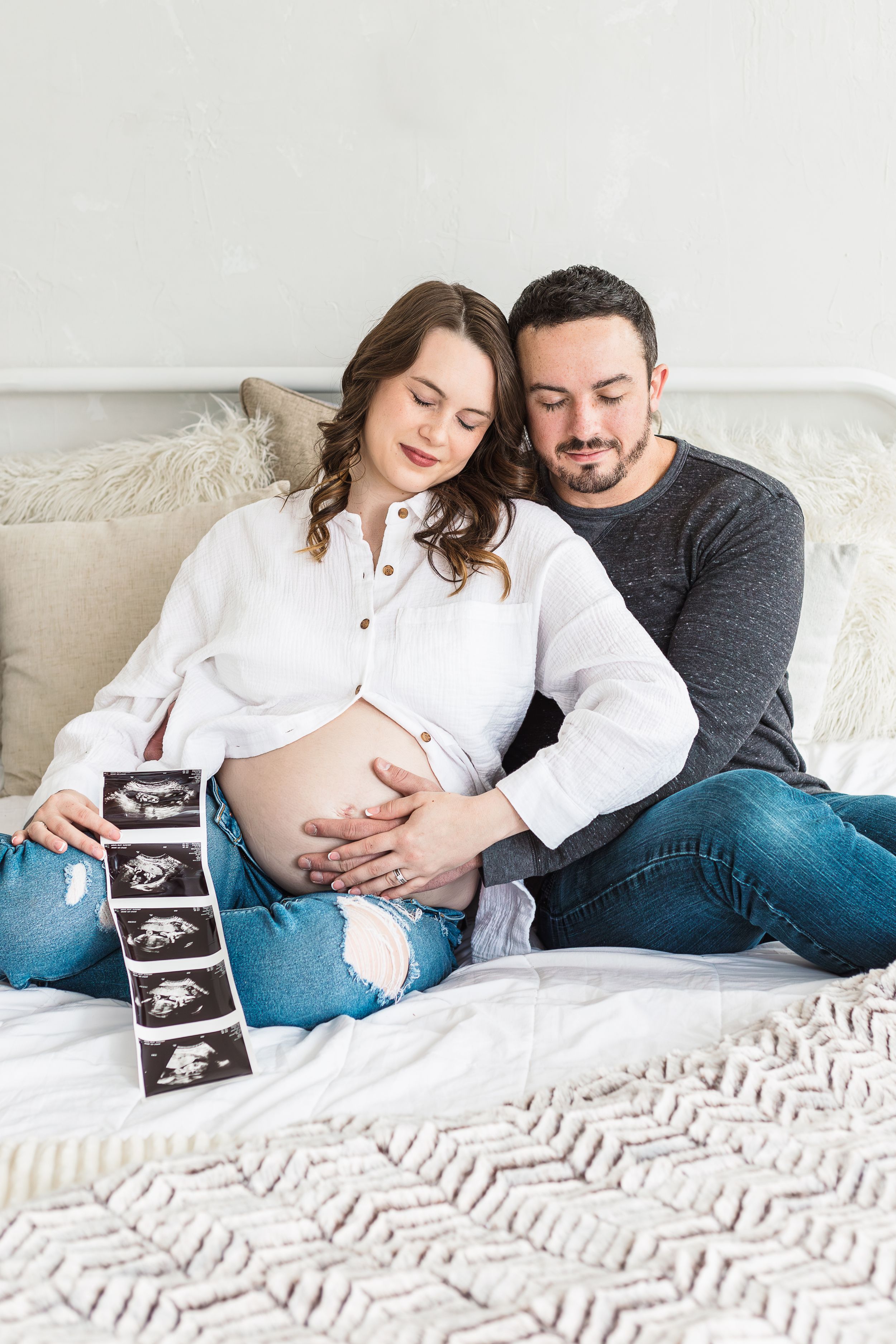Couple shares intimate moment with ultrasound photos on cozy white bedding.