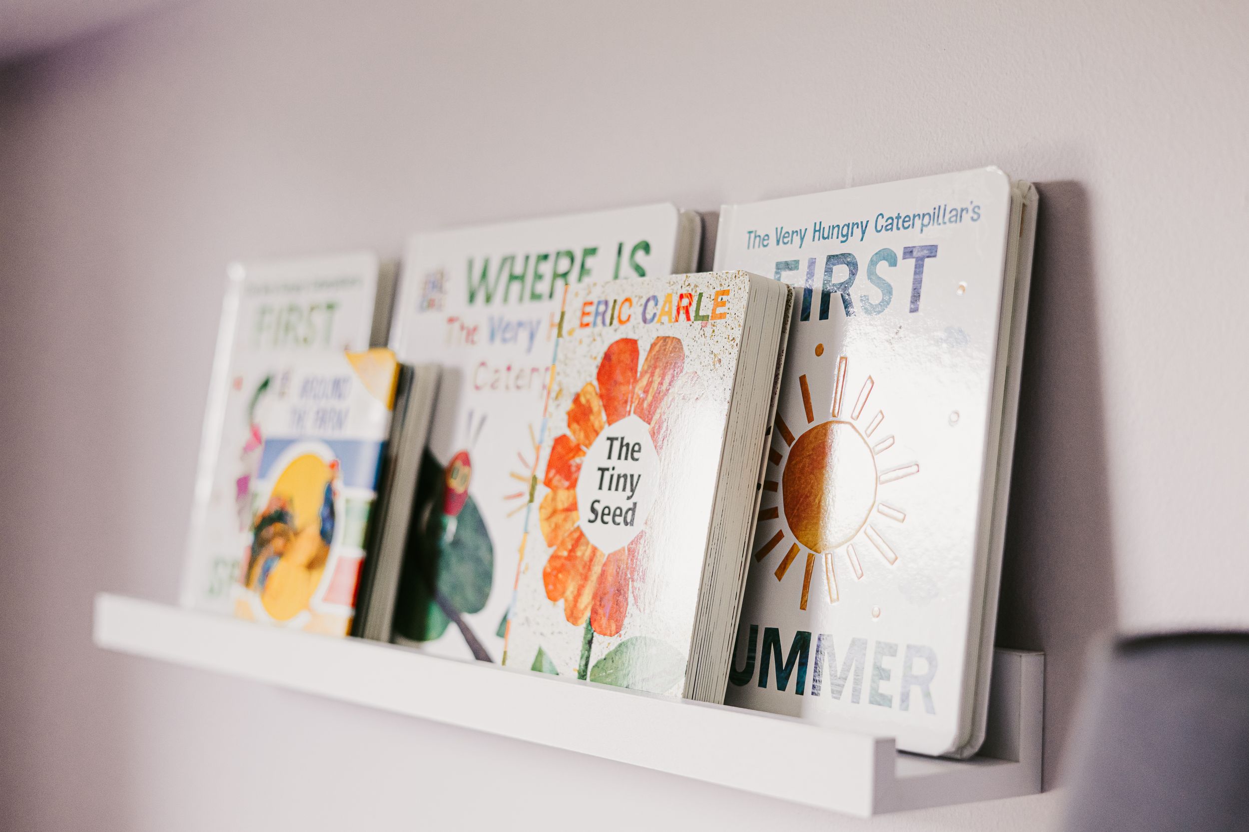 Children's books displayed on floating white shelf against pale wall.