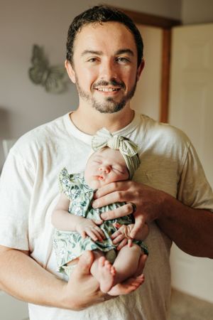 Parent holding a newborn baby wearing mint green floral outfit.