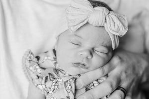 Sleeping newborn baby wearing white bow headband in black and white portrait.