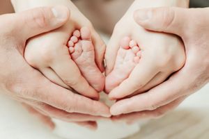 Tiny newborn feet held in adult hands forming heart shape.