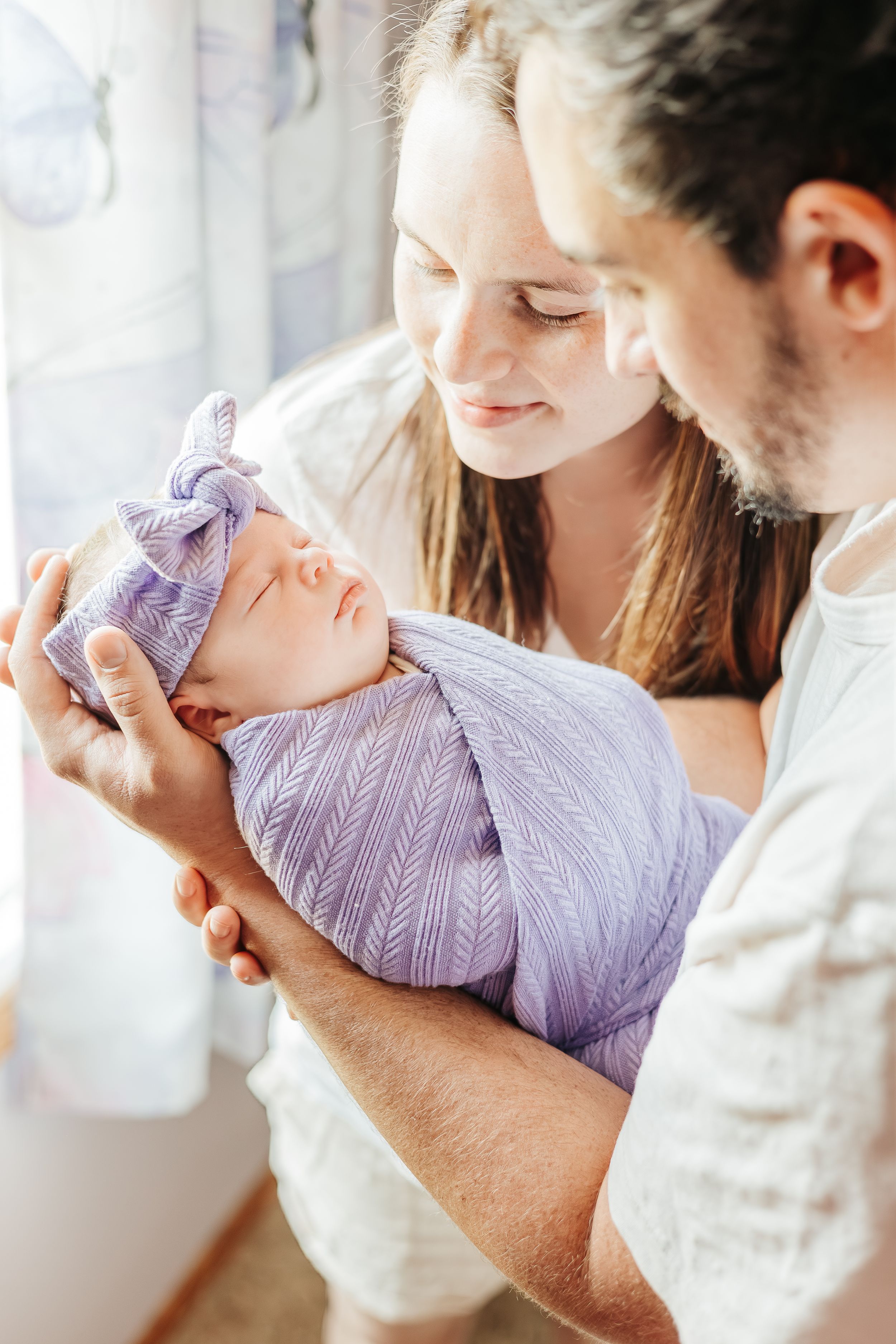 Newborn baby wrapped in purple swaddle with matching bow headband.