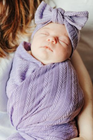 Sleeping baby wrapped in purple textured swaddle with matching bow.