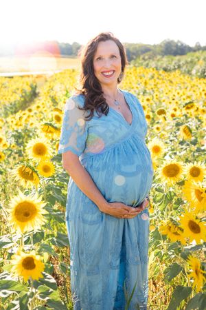 Someone in a flowing blue dress poses amid a vibrant field of bright yellow sunflowers in the golden sunlight.