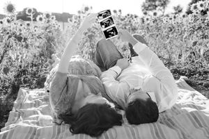 A black and white romantic photo of a couple lying on a picnic blanket reading together in a flower field.