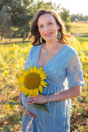 A person in a blue lace dress poses in a sunflower field during golden hour.