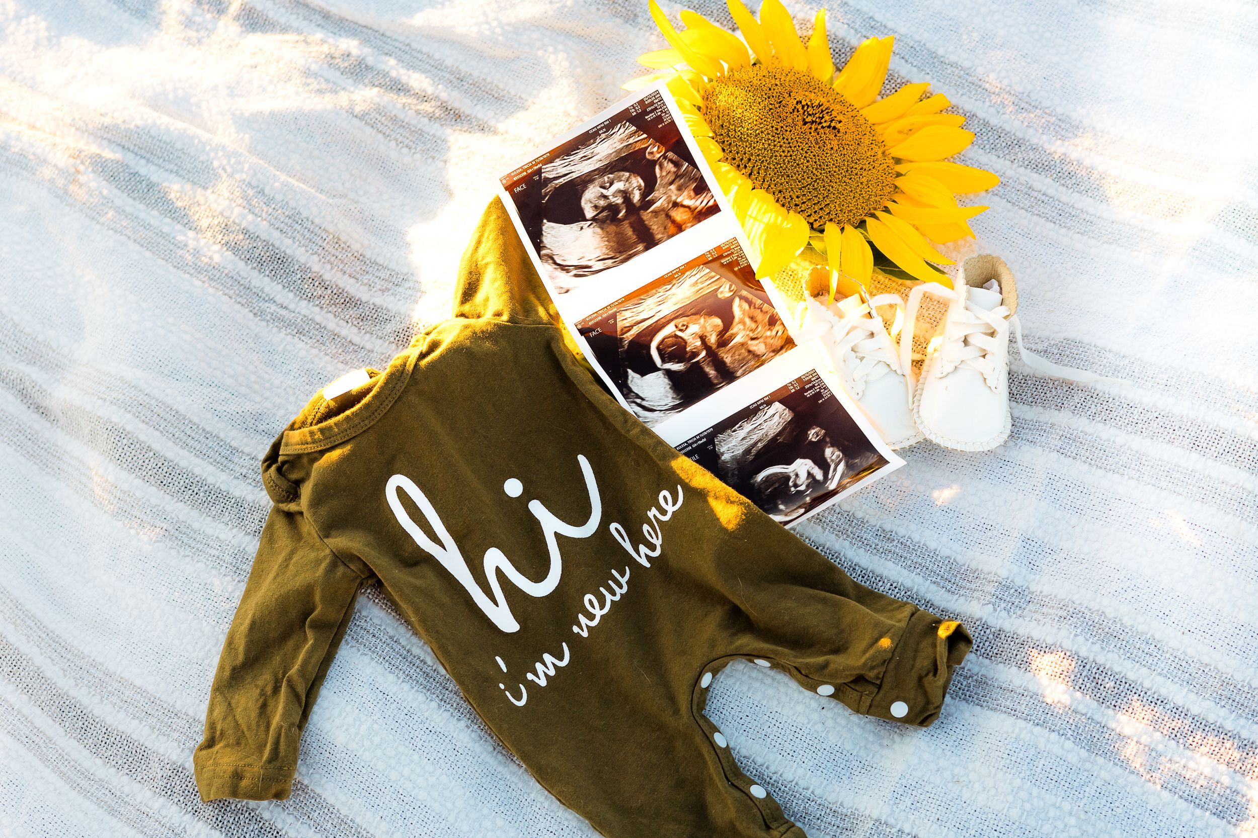 Baby ultrasound photos displayed with a sunflower and green 'hi' onesie for a pregnancy announcement.