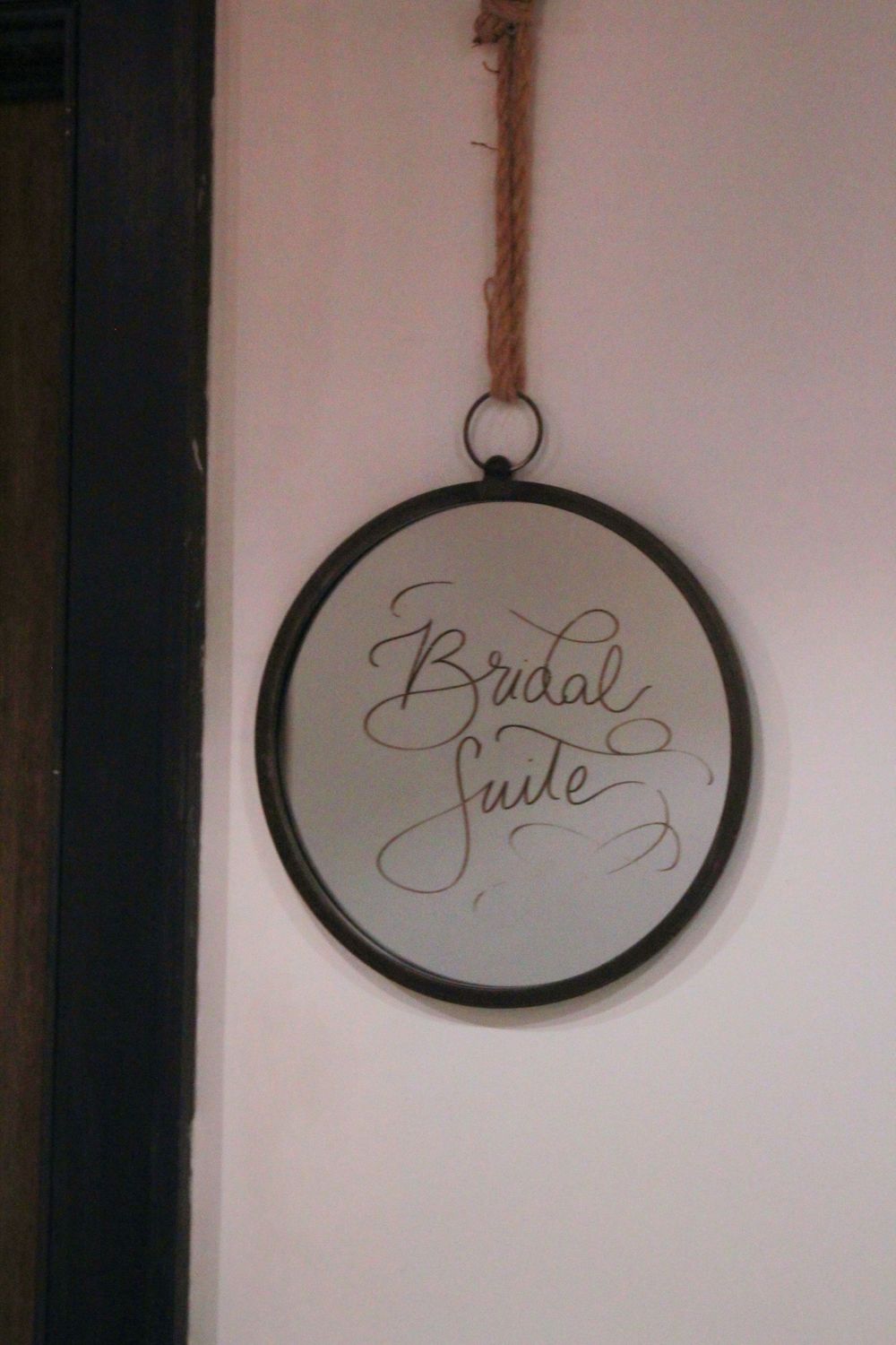 Round mirror with 'Bridal Suite' text hanging on light pink wall.