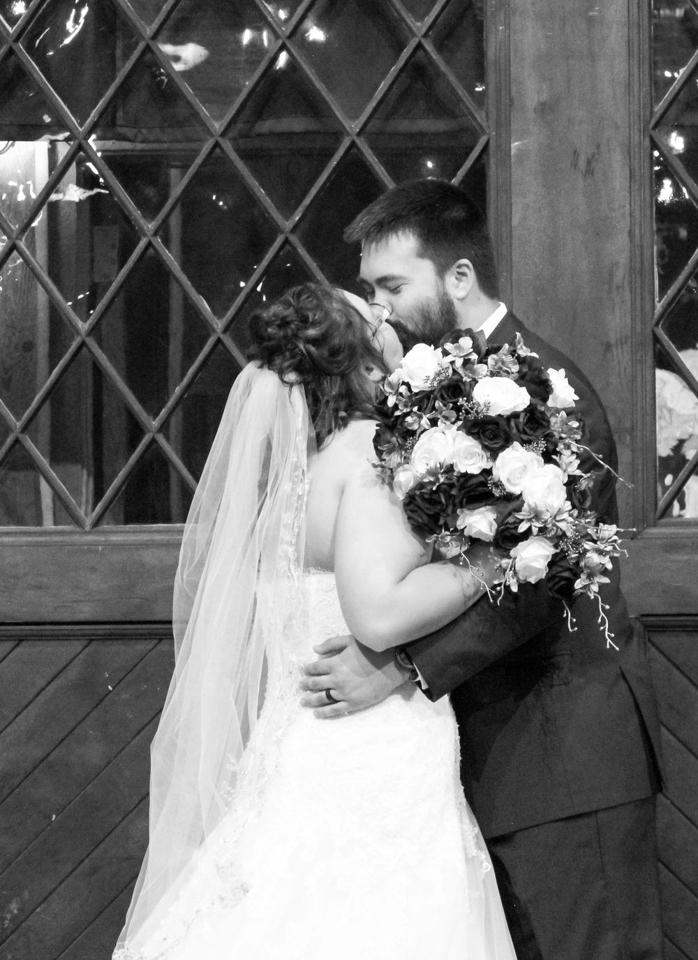 Romantic black and white portrait of newlyweds embracing with floral bouquet.