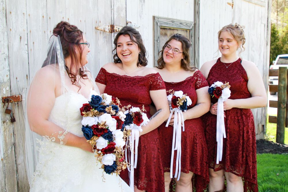 Wedding party in burgundy dresses holding blue and white bouquets outdoors.