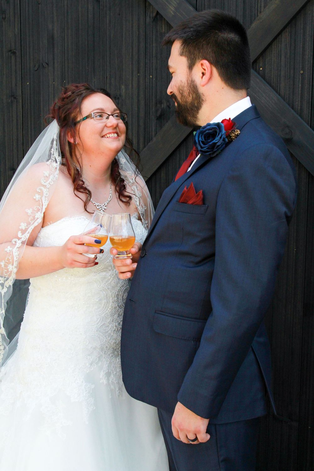Newlyweds share drinks and smiles against a dark wooden backdrop.