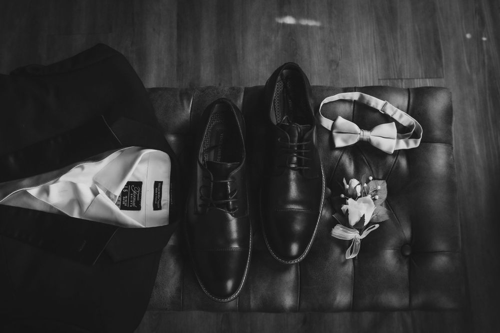 Black dress shoes and bow tie arranged on dark wooden surface for wedding preparation.