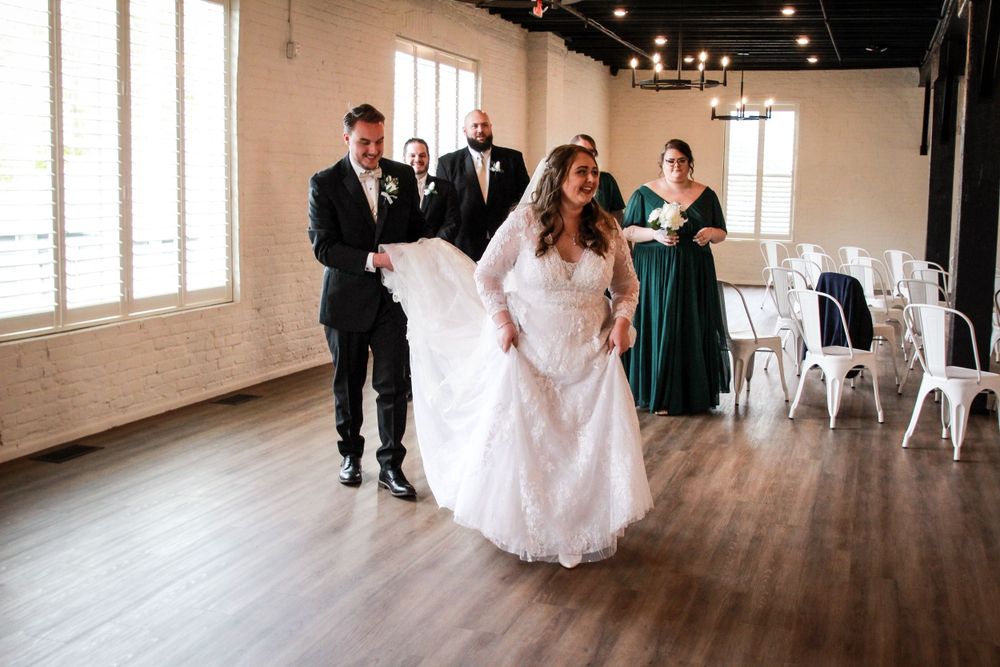 Wedding party helping with a bride's dress in an industrial-style venue with white chairs.
