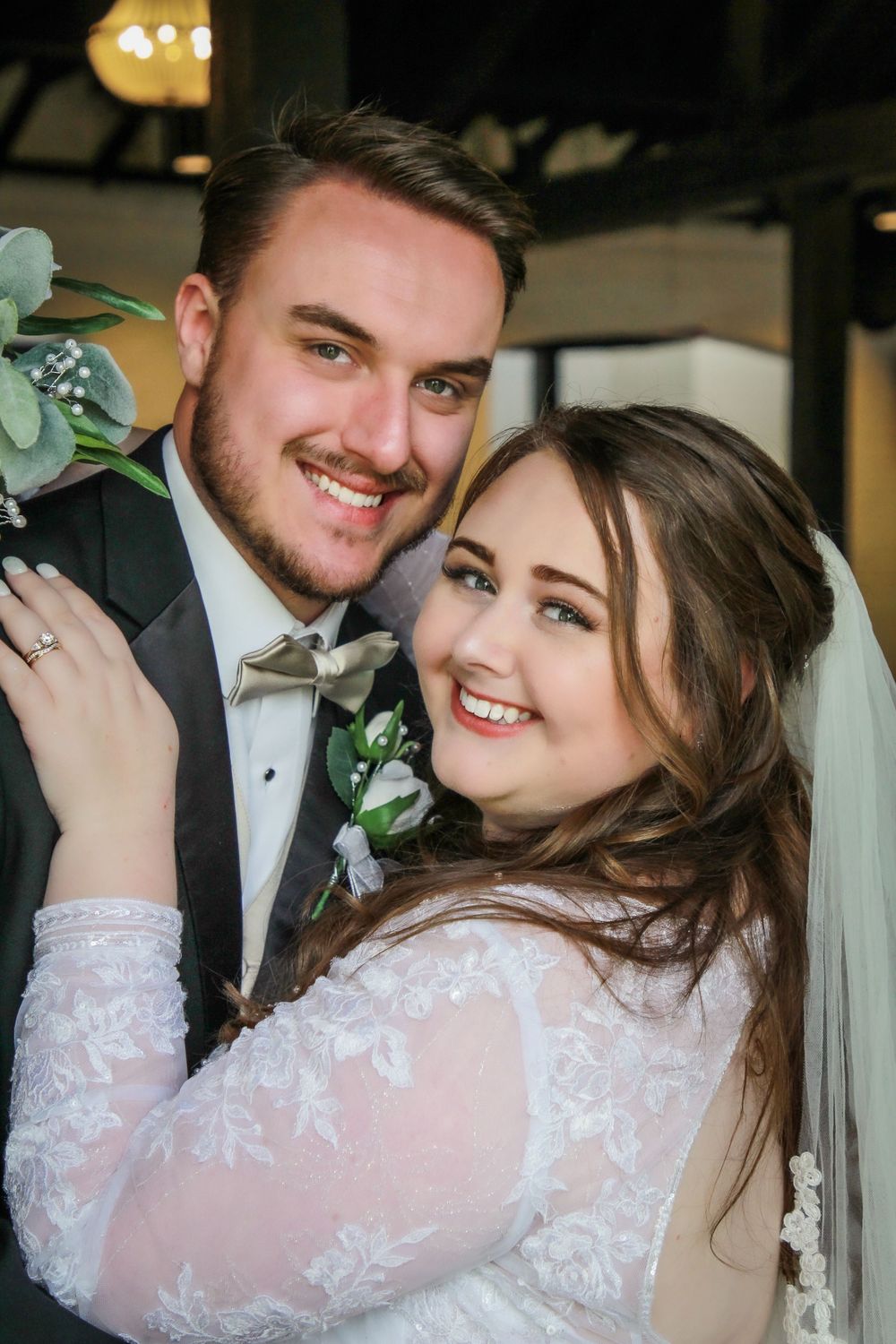 A wedding portrait featuring a couple in formal attire with eucalyptus decor.