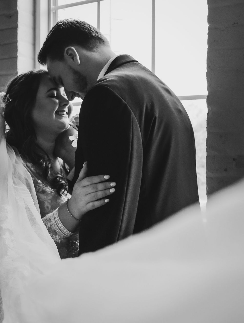 An intimate black and white wedding moment captured near a window.