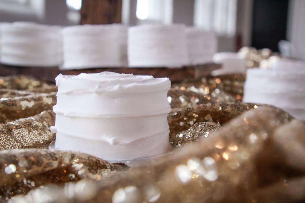 White frosted mini cakes lined up on a sparkly gold textured surface.