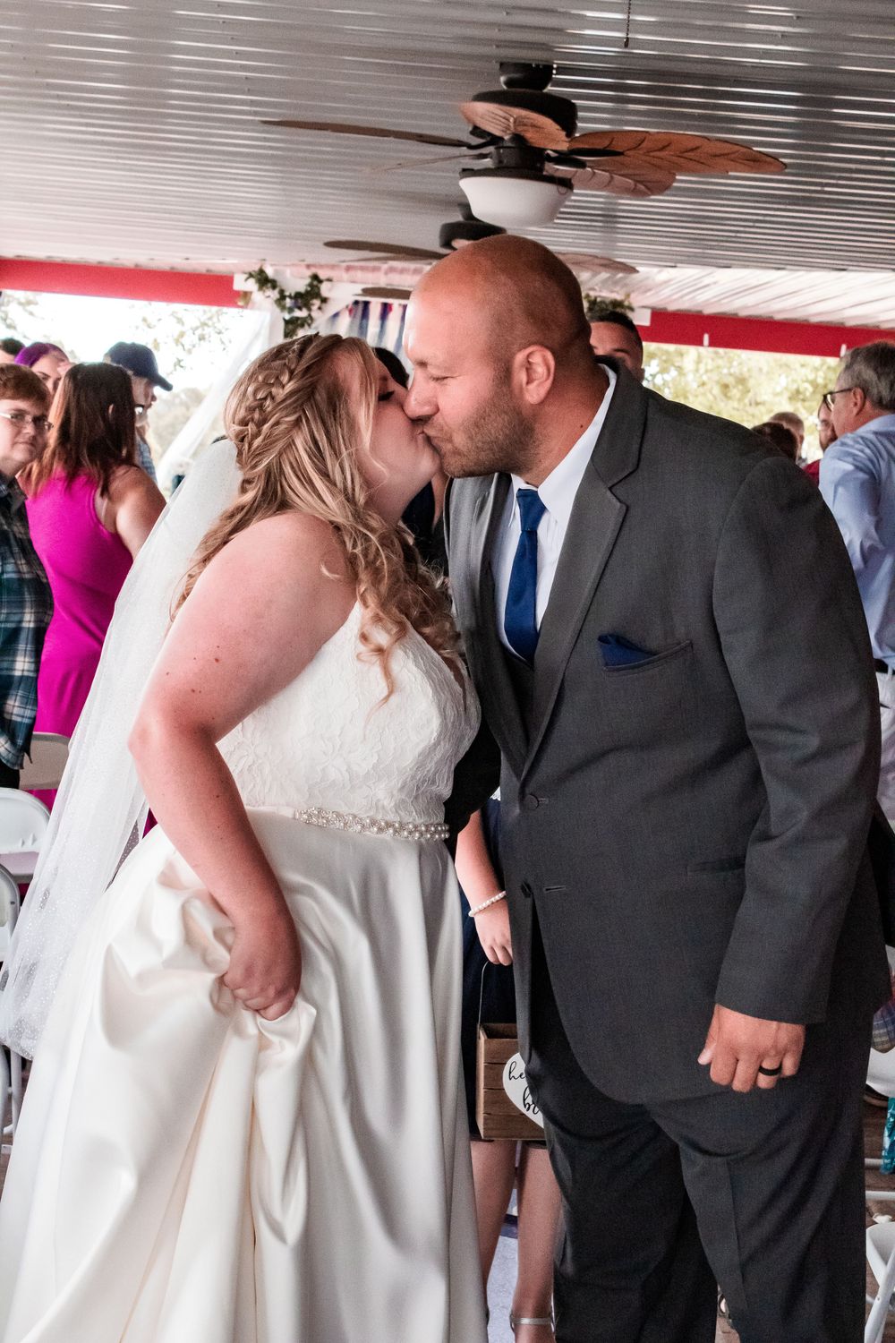 An intimate wedding kiss captured under a ceiling fan during an indoor reception.
