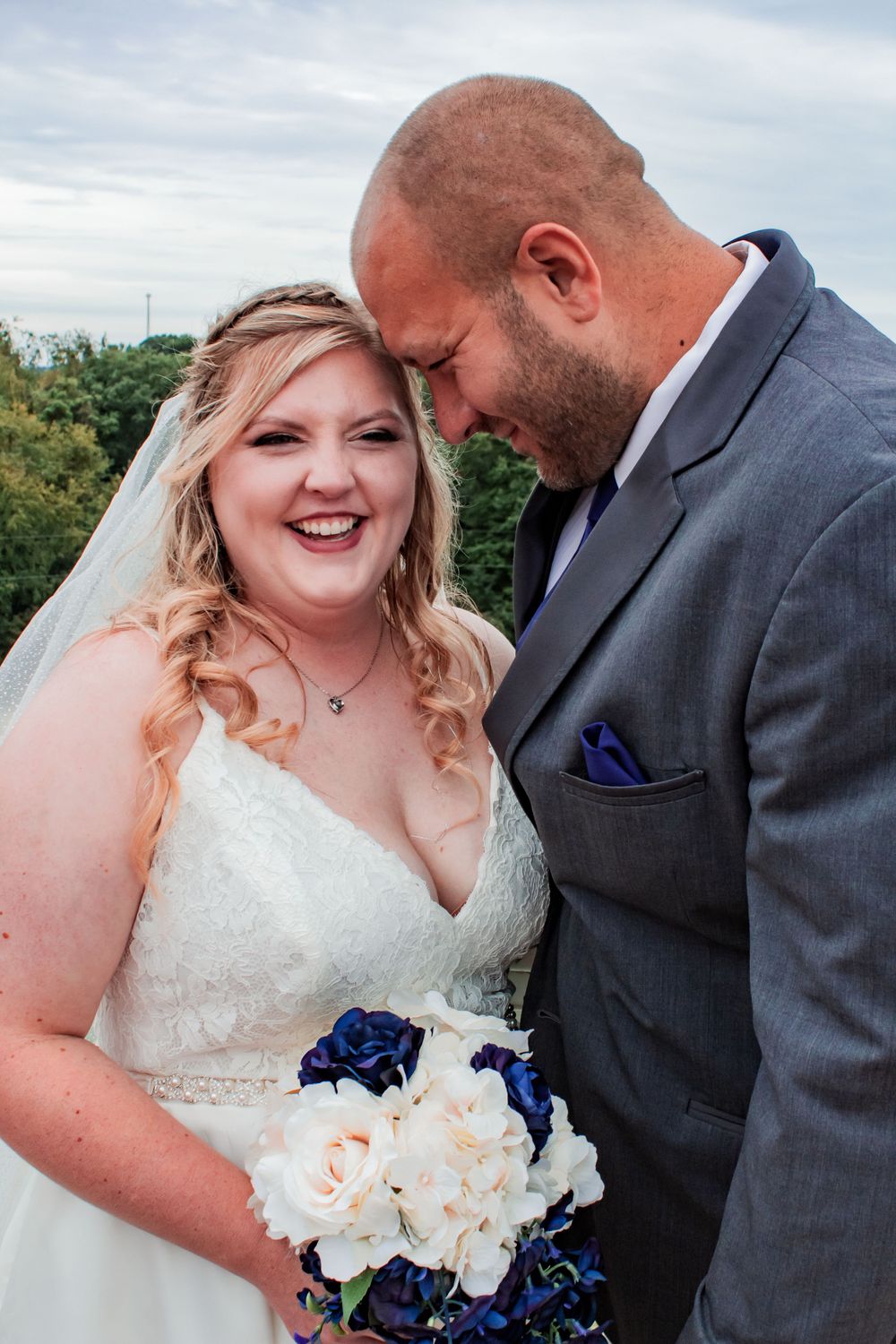 A joyful moment shared between a bride in a white lace gown and groom in a dark suit holding a blue and white bouquet.
