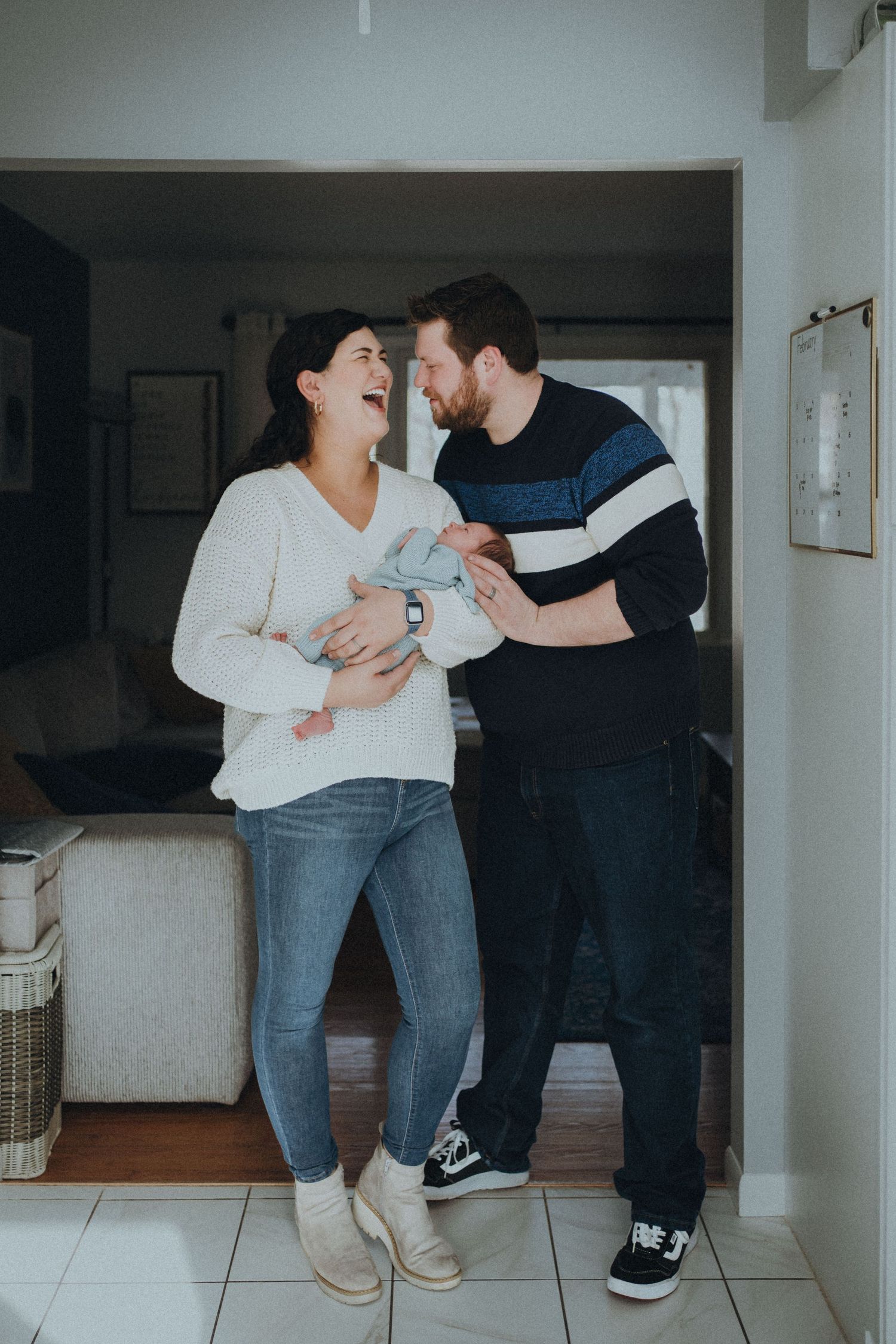 Candid moment of joyful parents laughing while holding their newborn in a home setting.