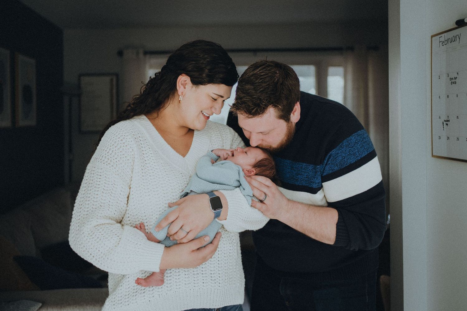 Intimate indoor portrait of new parents tenderly gazing at their newborn baby.
