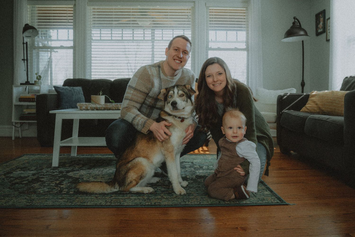 Family sits together with their German Shepherd dog on a gray rug in a cozy living room.