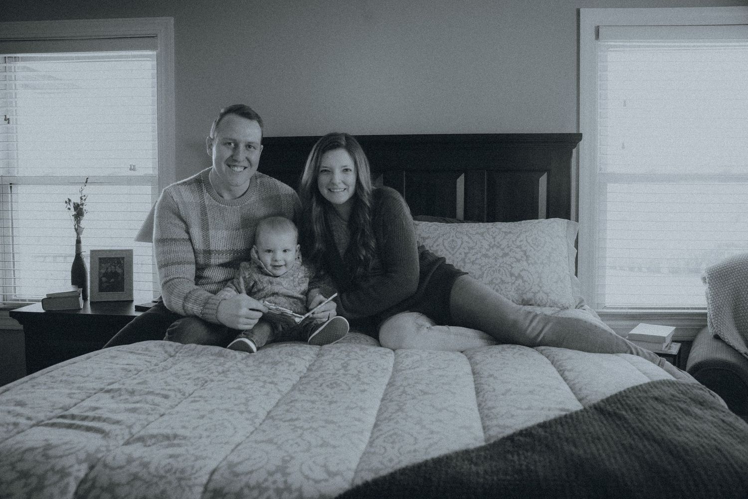 A family relaxes together on a bed in a casual black and white photograph.