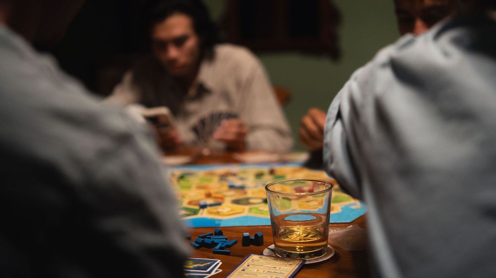 Friends gathered around a dimly lit table playing board games and enjoying snacks together.