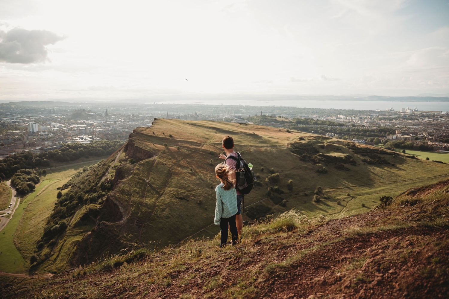 A couple enjoys the panoramic view from Arthur's Seat overlooking Edinburgh's cityscape.
