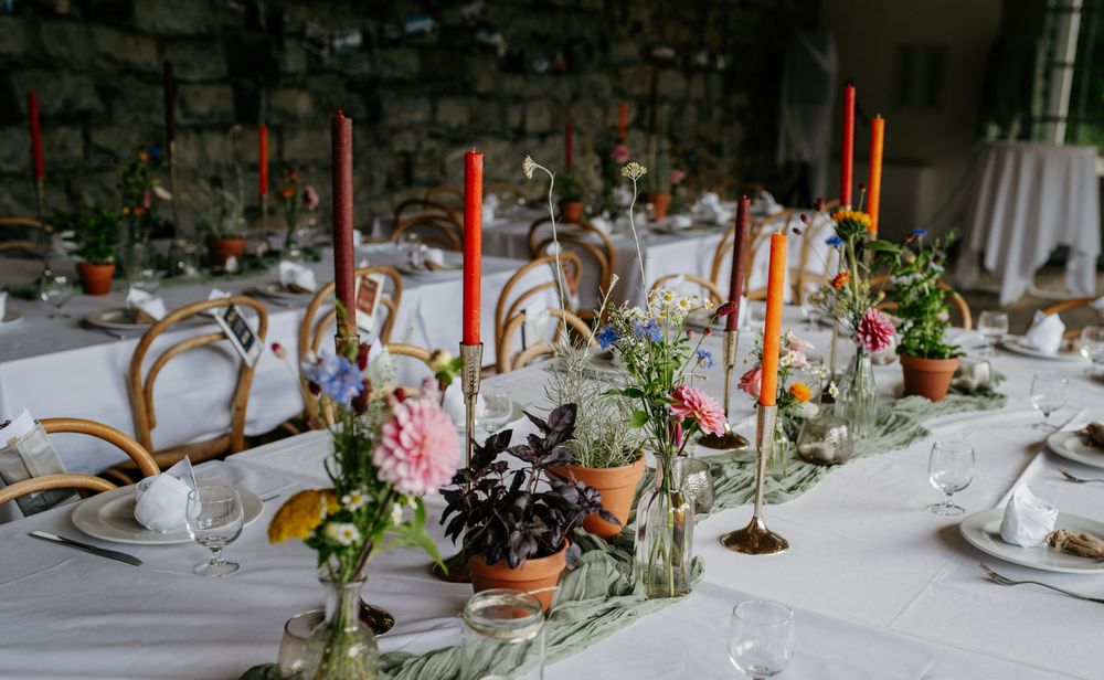 Vibrant wedding table centerpiece with colorful flowers and tall orange taper candles.