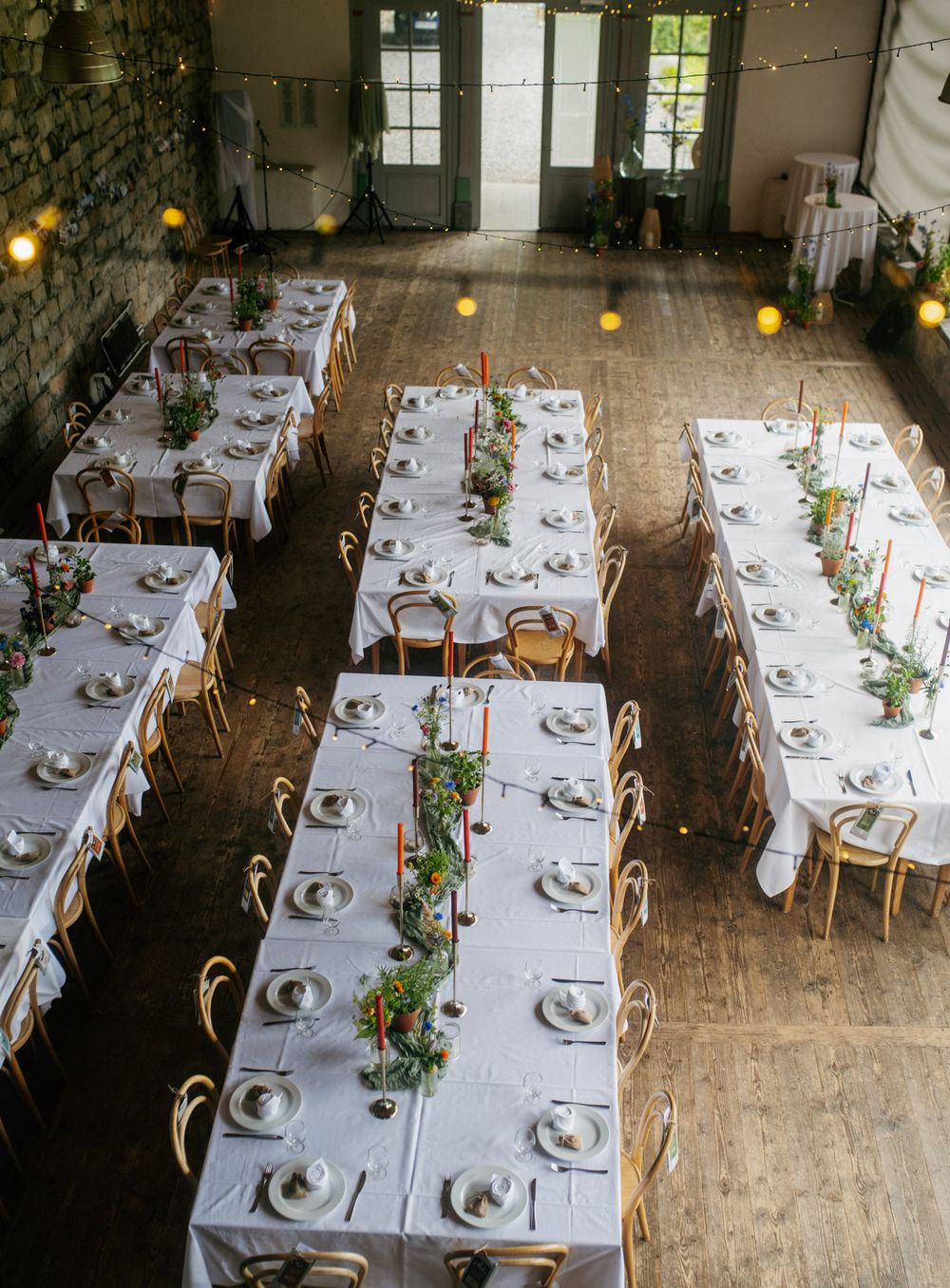 Aerial view of elegant wedding reception hall with long white-clothed tables adorned with greenery garland centerpieces.