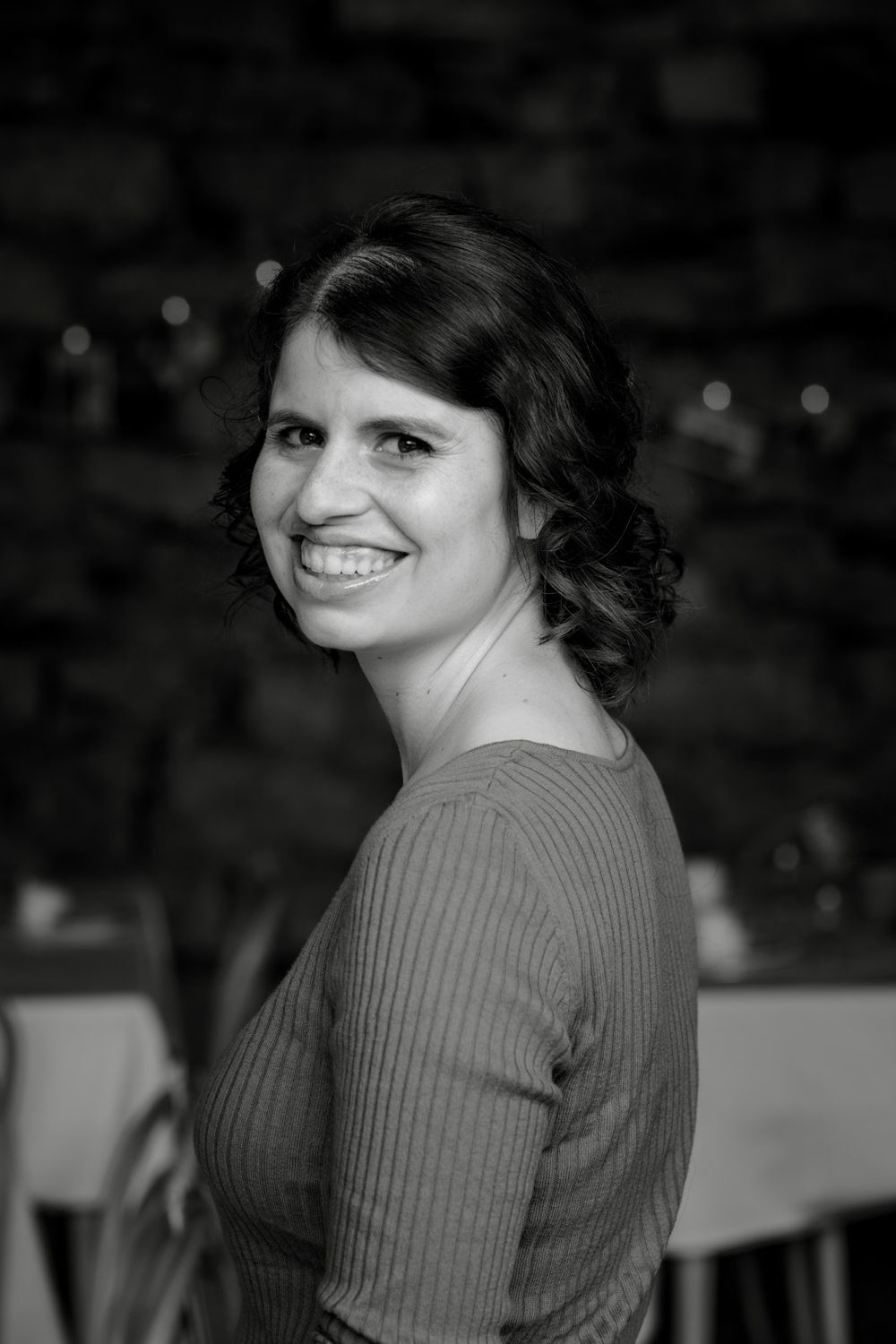 Black and white portrait of a smiling dark-haired woman in a ribbed top at a wedding reception venue.