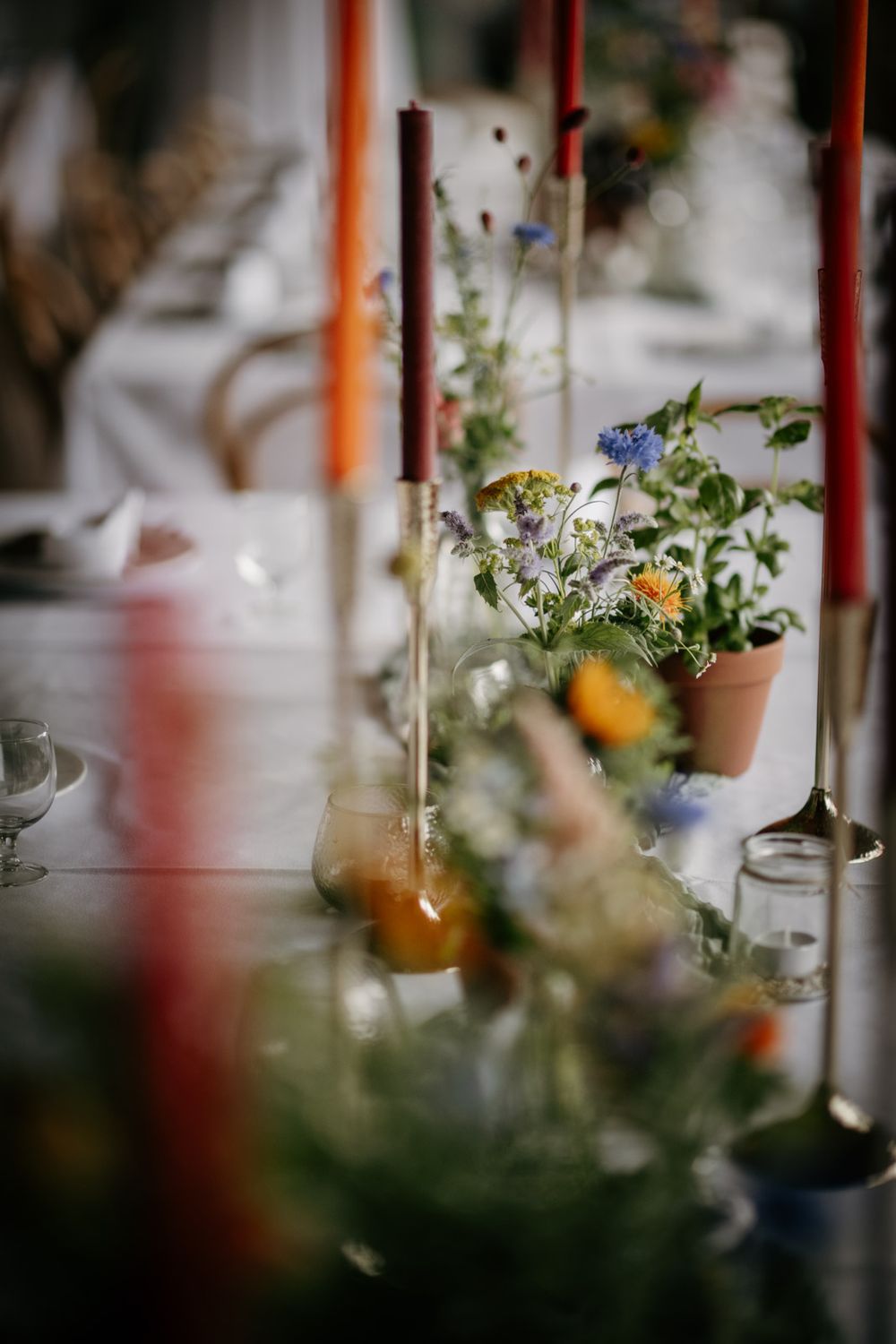 Colorful wildflower centerpieces with tall orange candles on white wedding table.