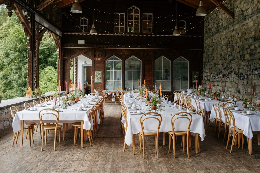 Rustic wedding reception venue with long white tables and bentwood chairs indoors.