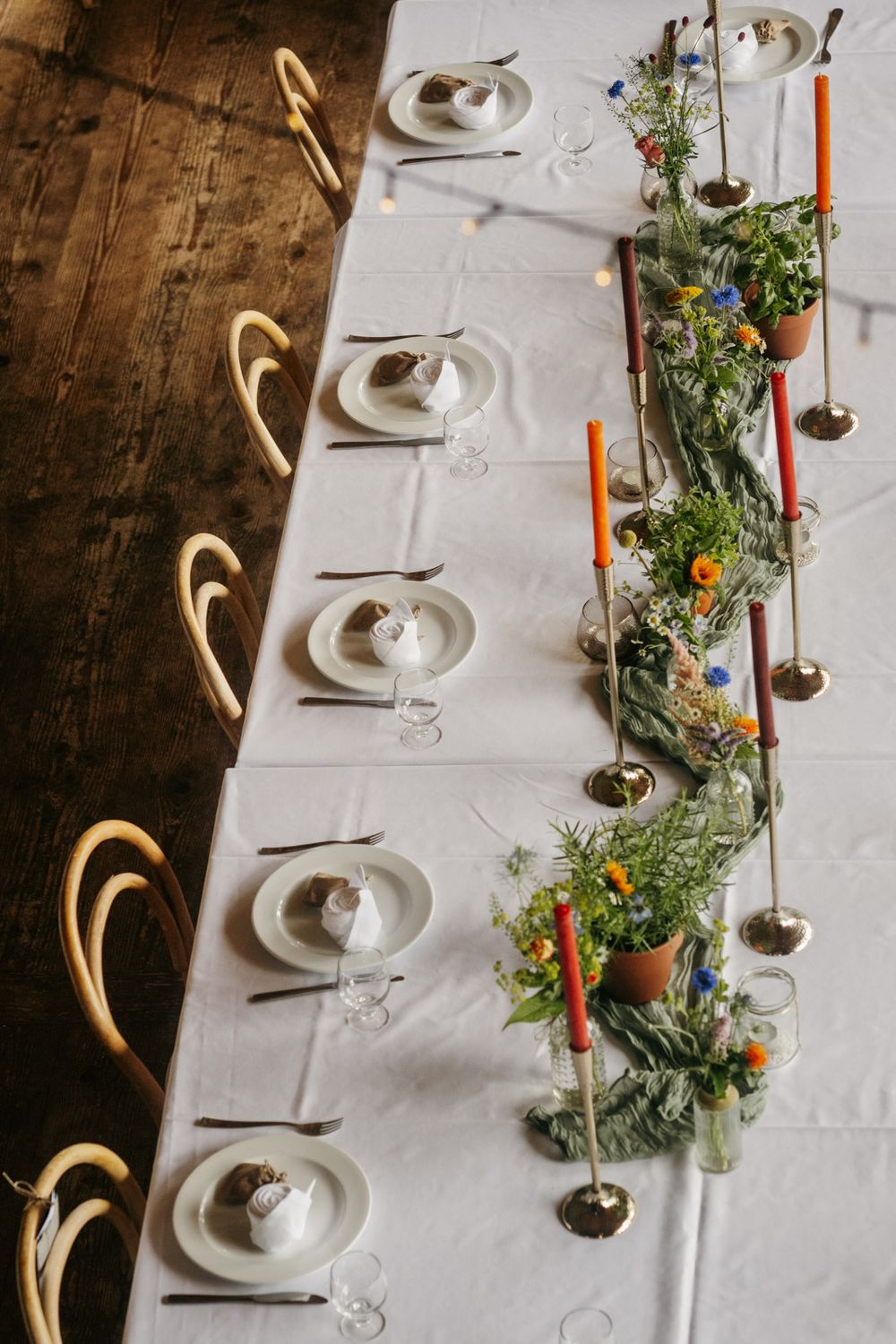Overhead view of elegant wedding table with orange candles and wildflower arrangements.