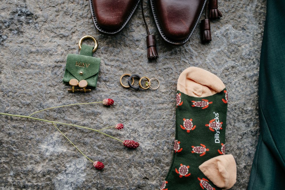 Groom wedding accessories flatlay with green socks, rings, shoes, and green wallet.